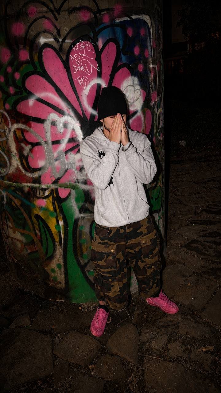 German Wasteland grey Sigil Zip-Up Hoodie editorial photo with camouflage cargo pants, pink sneakers and graffiti wall location